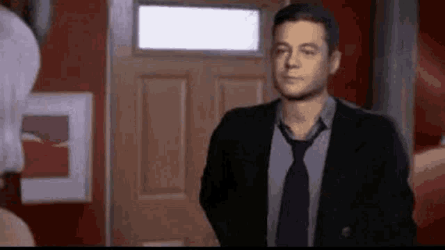 a man in a suit and tie is standing in front of a door and talking to a woman .