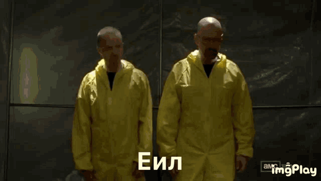 a man in a yellow coverall stands next to another man in a yellow coverall with the letters e and i on them
