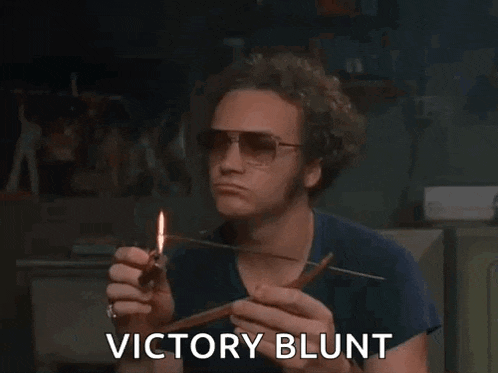 a man wearing sunglasses is lighting a cigarette with a lighter and says `` victory blunt '' .