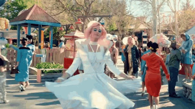 a woman in a white dress with pink hair is dancing in a crowd of people