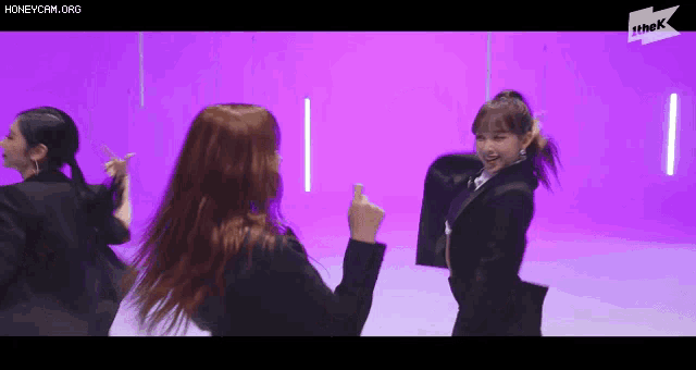 a group of women are dancing in front of a purple wall .