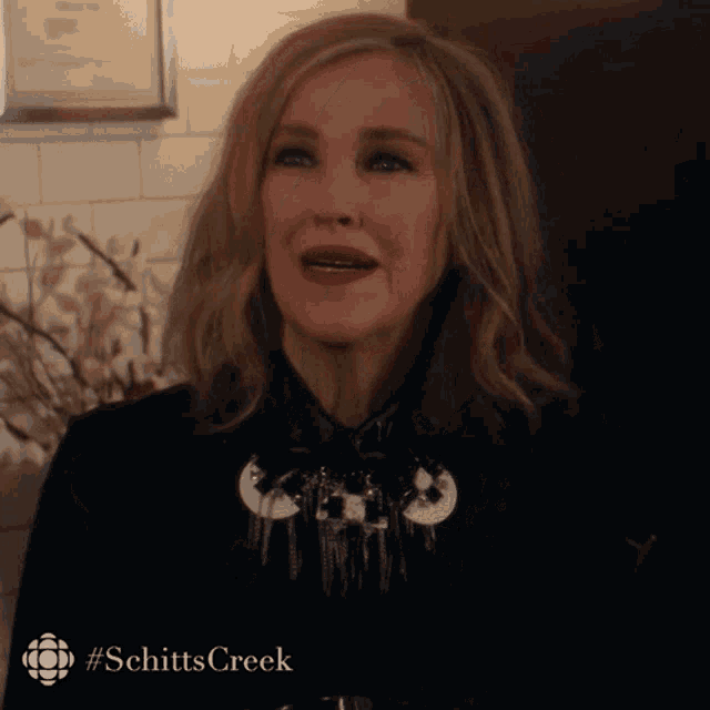 a woman wearing a black jacket and a necklace with the hashtag schitts creek on the bottom