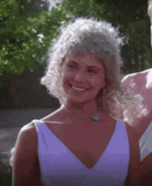a woman wearing a white dress and a blue necklace smiles