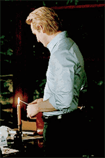 a man in a blue shirt is lighting a match in front of a candle