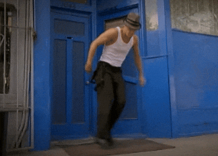 a man in a white tank top and black pants dancing in front of a blue door