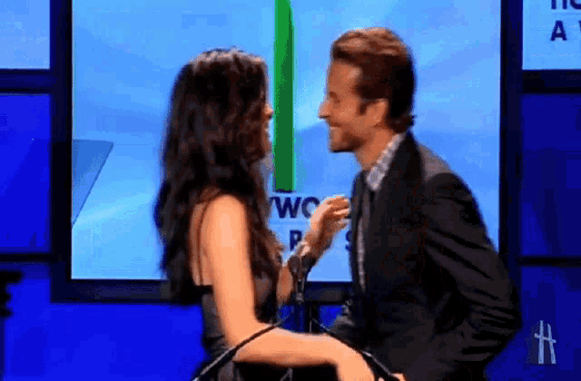 a man and a woman are kissing in front of a screen that says two