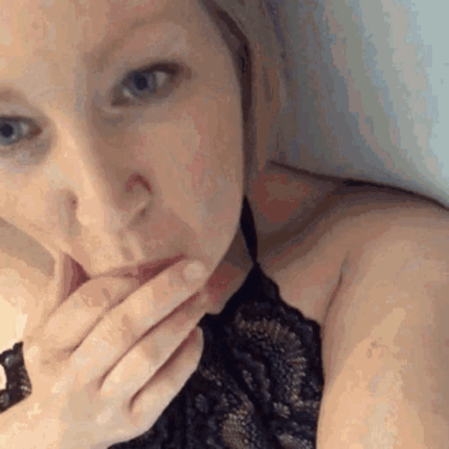 a woman in a black lace top is covering her mouth with her hands .