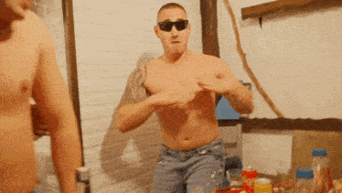 a shirtless man wearing sunglasses is standing in front of a table with coca cola cans