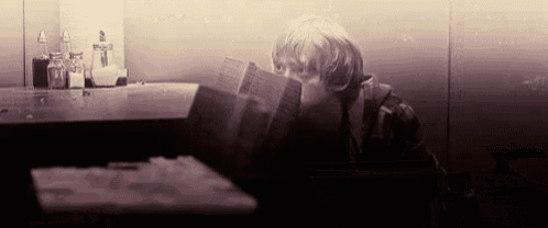 a young boy is reading a book while sitting at a table in front of a mirror .