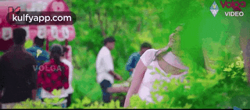 a group of people are standing in a park surrounded by trees and balloons .