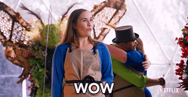 a woman wearing an apron is standing in front of a group of people and says wow .