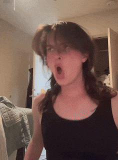 a woman in a black tank top is yawning in a bedroom