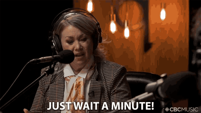 a woman wearing headphones says " just wait a minute " in front of a microphone