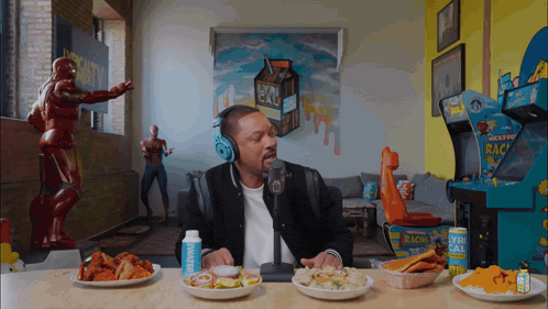 a man wearing headphones sits at a table with plates of food and a can of lucky strike