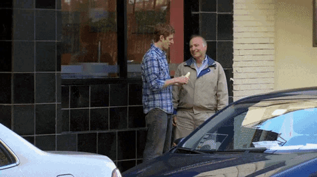 two men standing in front of a car talking