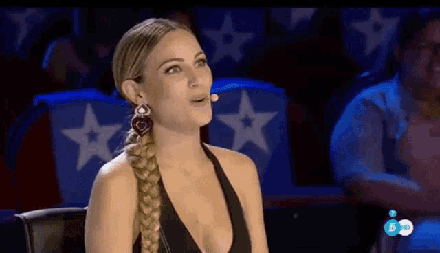 a woman wearing a braided ponytail and earrings is sitting in front of a microphone on a television show