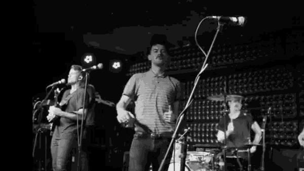 a man stands in front of a microphone in a black and white photo of a band