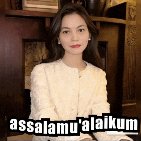 a woman in a white jacket is sitting in front of a sign that says assalamu'alaikum