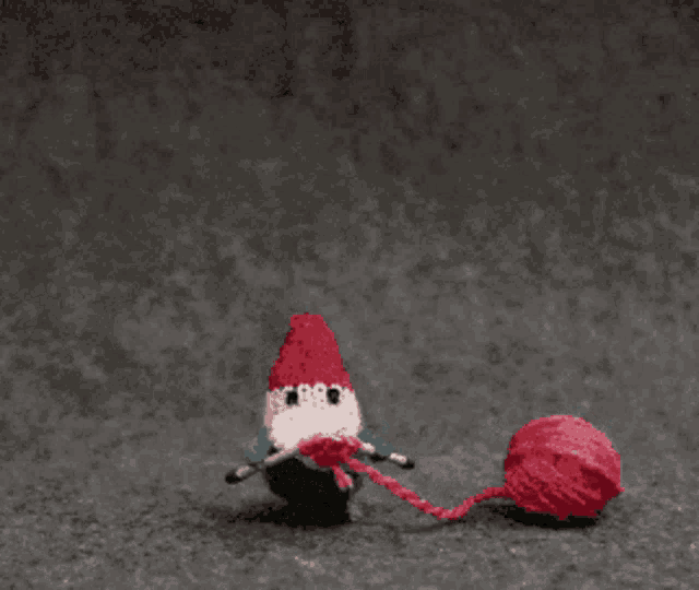 a stuffed animal with a red heart on its head is standing next to a red ball of yarn