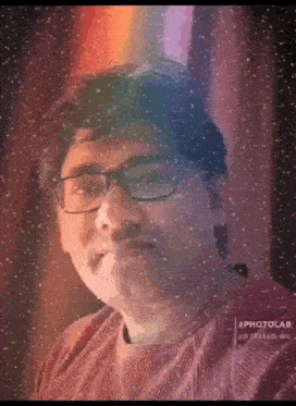 a man wearing glasses is standing in front of a window with snow falling on him .