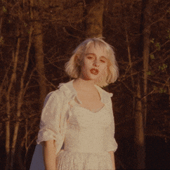 a blonde woman in a white dress is standing in the woods