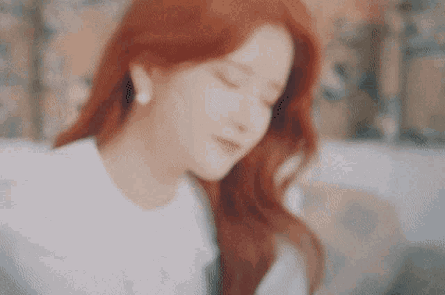 a woman with red hair is sitting on a couch with her eyes closed and wearing earrings .