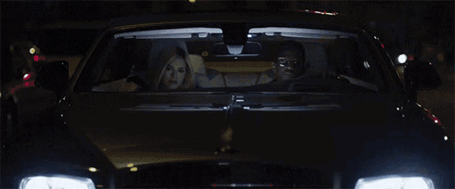a car with the headlights on is driving down a street at night
