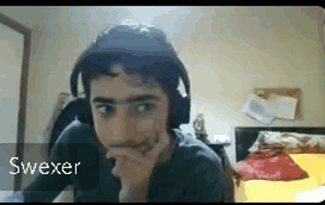 a young man wearing headphones is sitting in a bedroom with his hand on his chin .