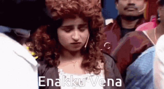 a woman with curly hair is standing in a crowd with the words enakku vena written on the bottom of her face .