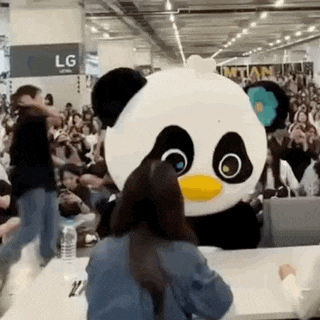 a panda mascot is standing next to a woman in front of a crowd .