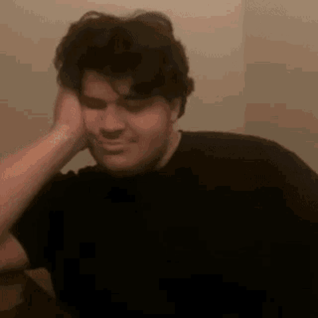 a man in a black shirt is holding his head in his hand .