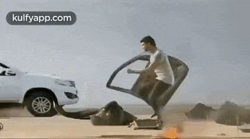 a man is kicking another man in the face while a car is driving past .