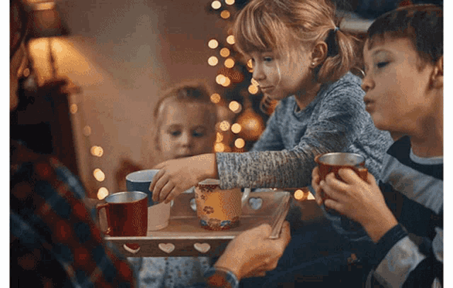 a group of children are sitting around a table with a tray of cups on it
