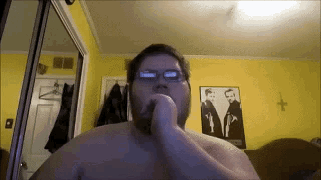 a shirtless man wearing glasses is sitting in front of a yellow wall ..