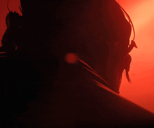 a close up of a person 's face in a dark room with a red background