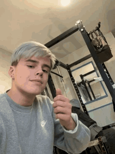 a young man wearing a grey nike sweatshirt is holding something in his right hand