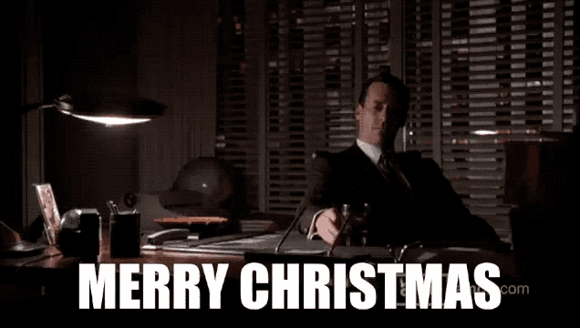 a man in a suit sits at a desk with the words merry christmas written above him