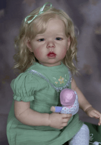 a baby doll in a green dress holds a pink doll