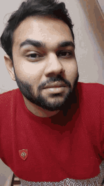 a man with a beard wears a red sweater with a shield on it