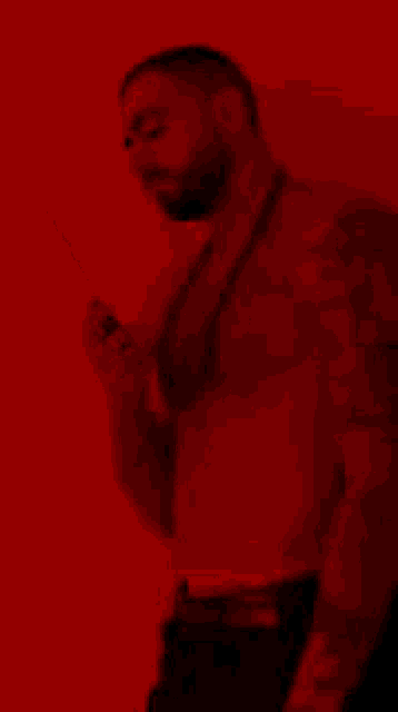 a shirtless man with tattoos is standing in front of a red wall .