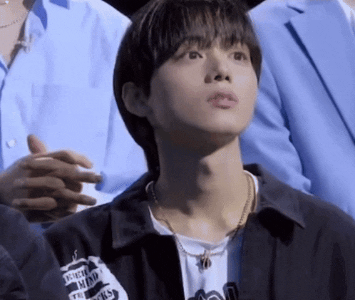 a young man wearing a black jacket and a necklace looks up