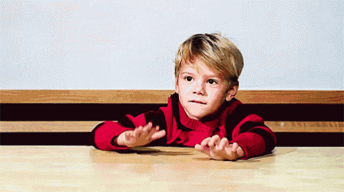 a little boy in a red sweater is sitting at a table with his hands outstretched