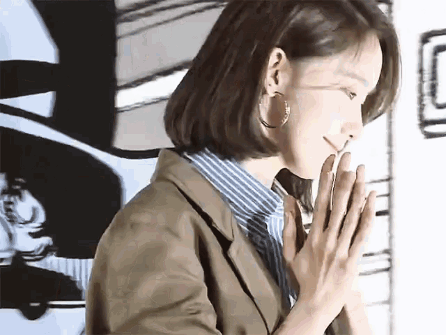 a woman wearing hoop earrings and a striped shirt is praying