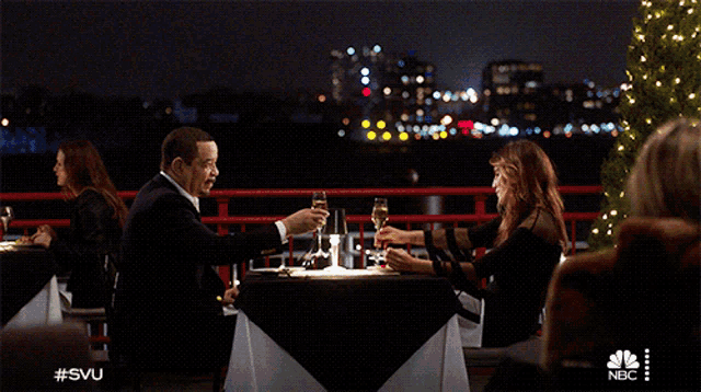 a couple toasting at a table with a nbc logo