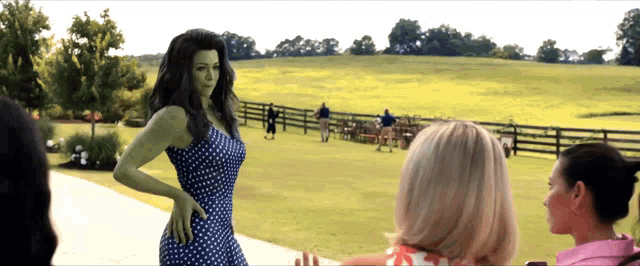 a woman in a polka dot dress is standing in front of a grassy field