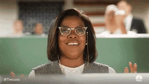a woman wearing glasses and headphones is smiling in front of a laptop computer .
