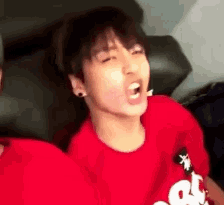 a young man in a red shirt is yawning while sitting on a couch .