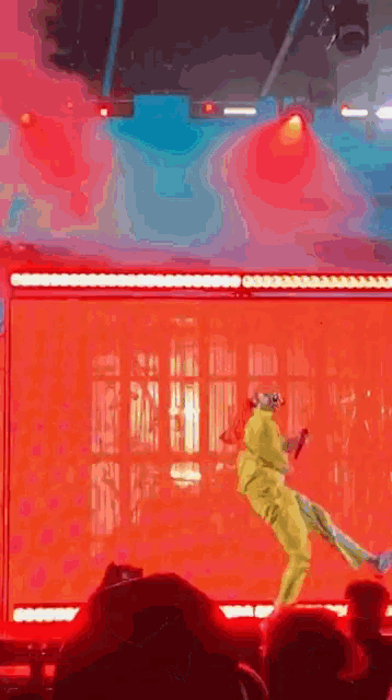 a man in a yellow suit is jumping in the air on a stage while holding a microphone .