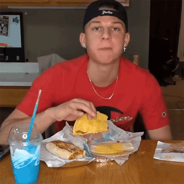 a young man wearing a red champion shirt is eating a taco