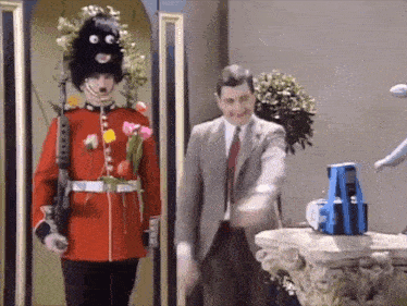a man in a suit and tie is standing next to a soldier in a red uniform with flowers in his pockets .